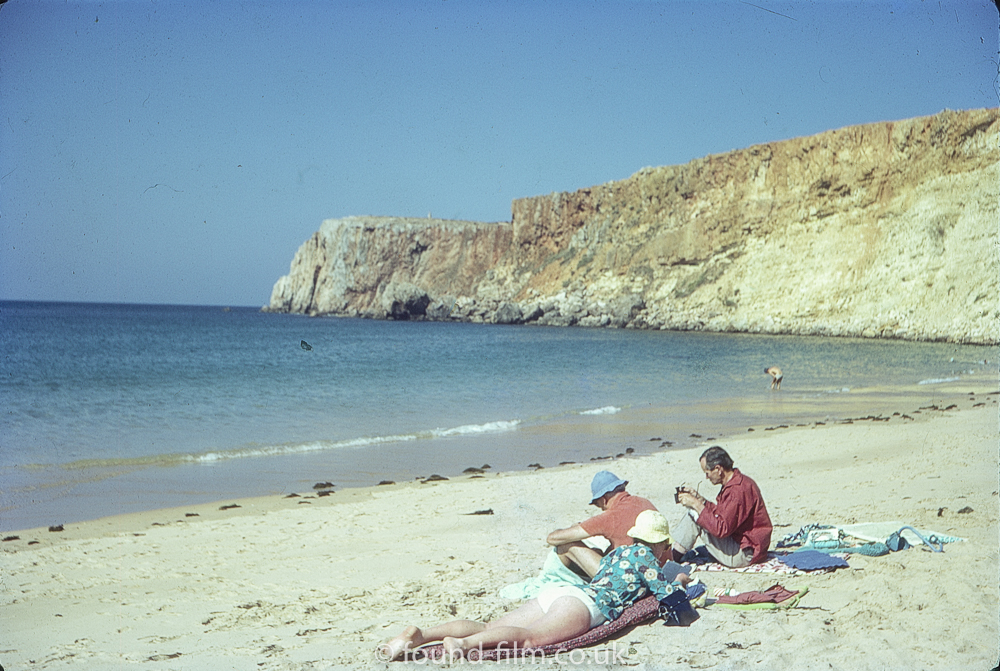Group sitting on a beach in the sunshine, August 1972
