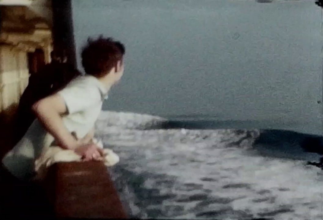 A still shot from a vintage home movie taken on a sea voyage showing a many looking across the sea from a ship