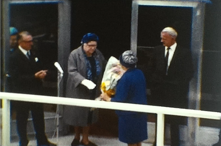 A still image from a standard 8 vintage home movie which shows an opening ceremony somewhere.