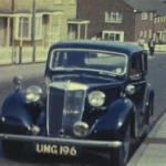 A still image from a vintage home movie featuring old cars.