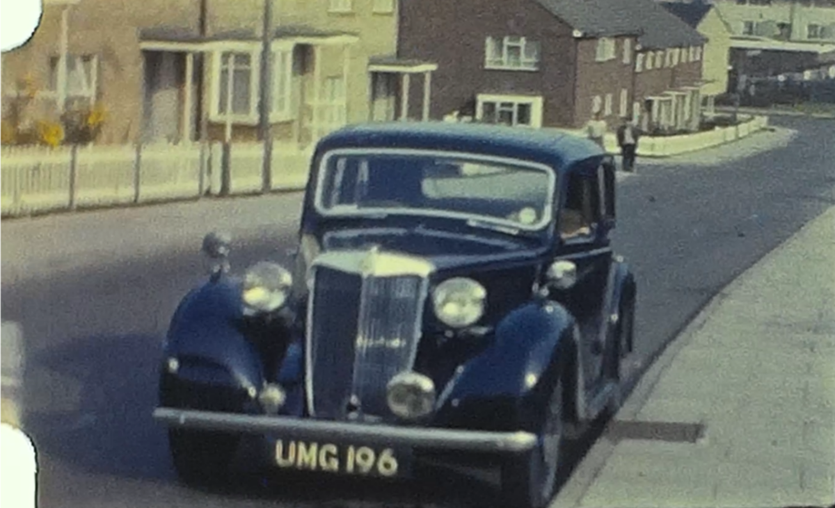 A still image from a vintage home movie featuring old cars.