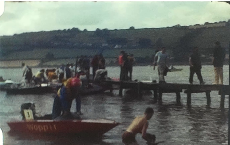 A still image from a vintage home movie which shows speed boats racing on a lake or waterway