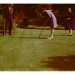 A still image from a vintage home movie featuring a family playing golf in their garden