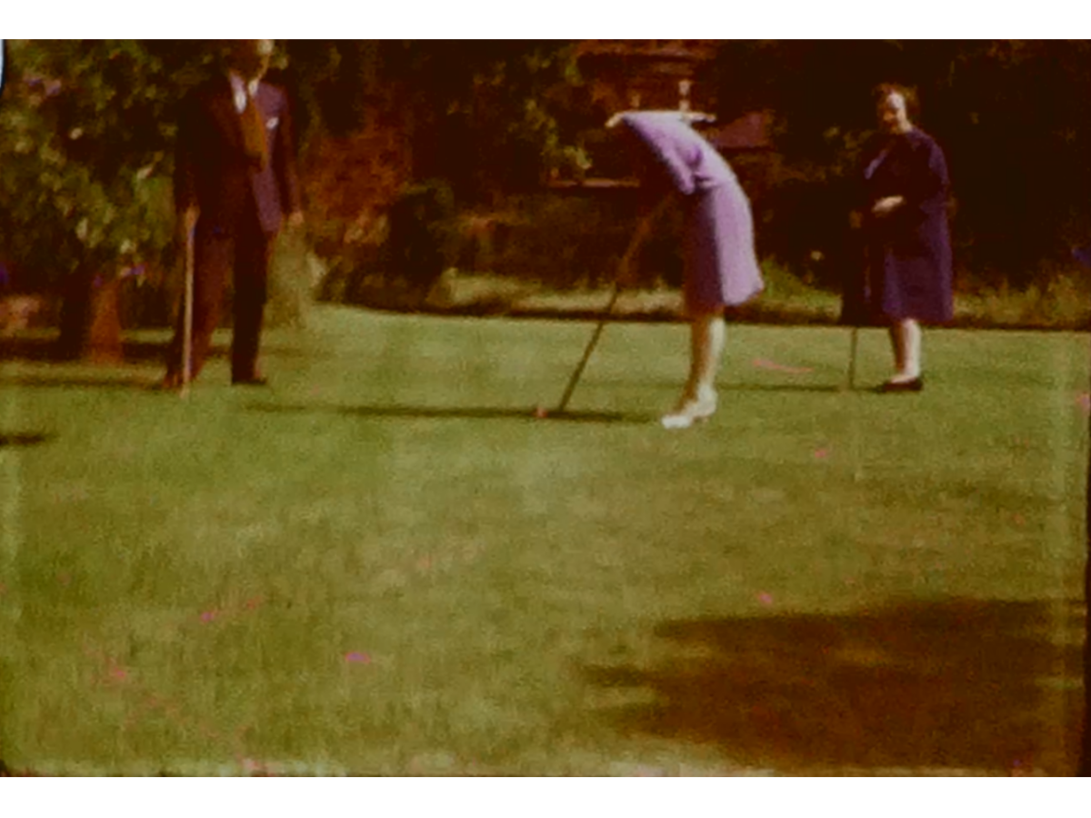 A still image from a vintage home movie featuring a family playing golf in their garden
