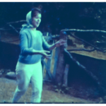 A still image from a vintage home movie which shows a young lady playing a game of catch in the garden
