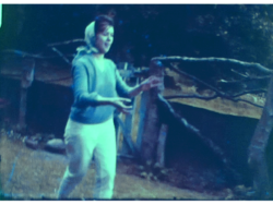 A still image from a vintage home movie which shows a young lady playing a game of catch in the garden