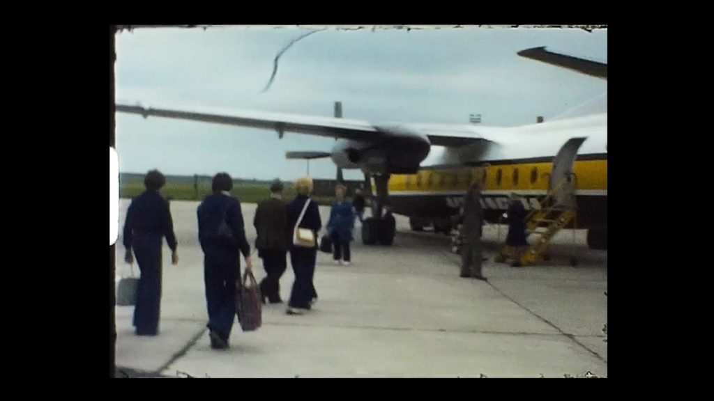 A still image from a Super 8 movie showing a family boarding a plane for Jersey