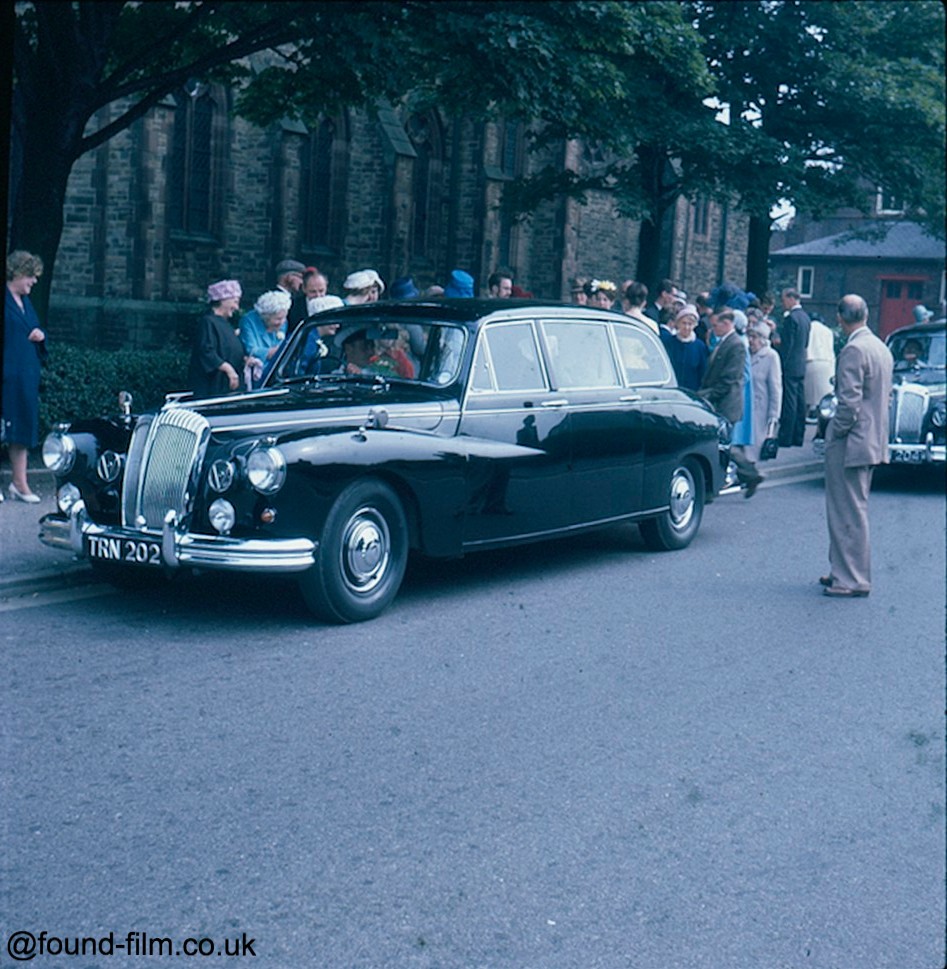 a group of people surrounding a car at a wedding