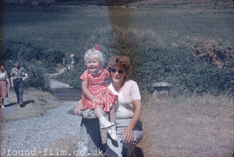 A little girl sits with her mother on a stone stool