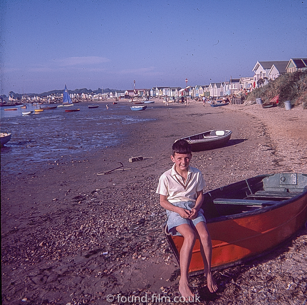A boy sitting on a dingy on a beach