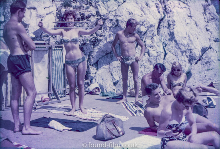 Girl in bikini building muscles on the beach, late 1950s