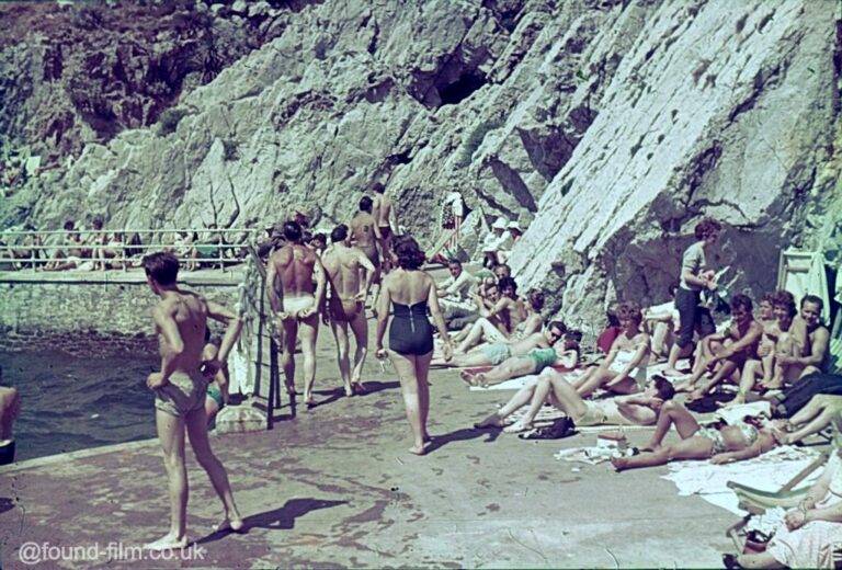 People sunbathing at the bottom of a rock face by the sea